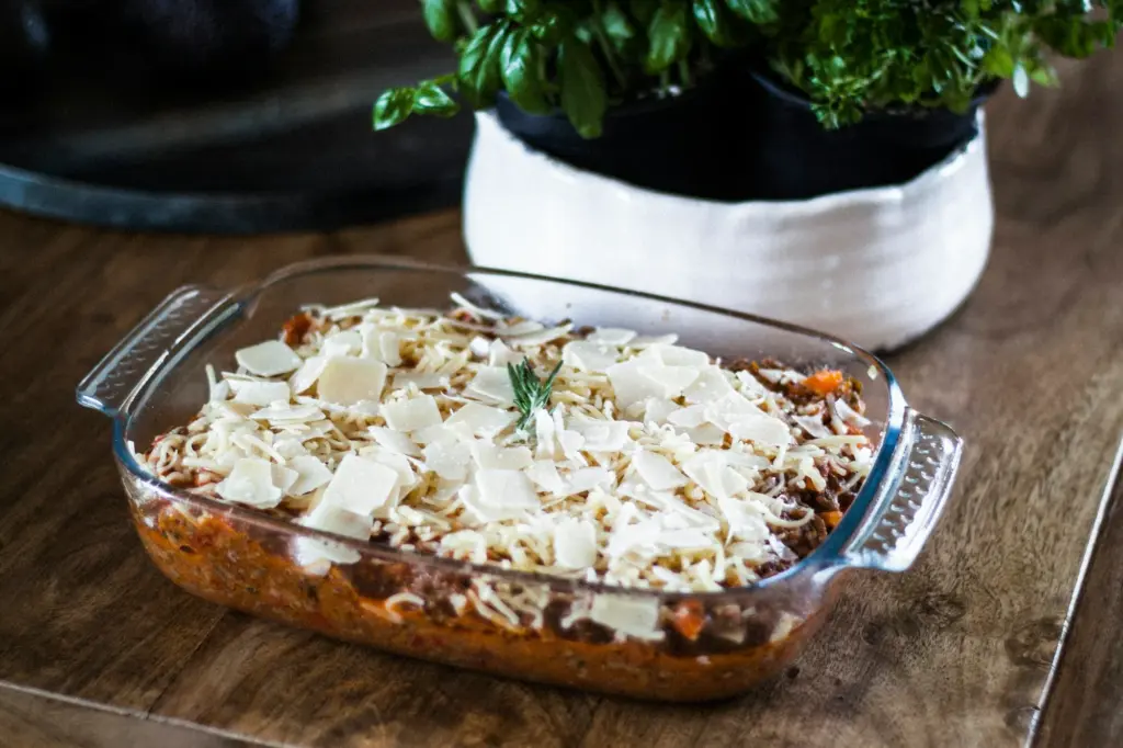 Unbaked casserole in a glass dish, layers of meat sauce covered with shredded and shaved white cheese