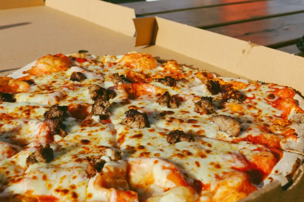 Cheese and sausage pizza, cut into slices, in an open plain cardboard pizza box