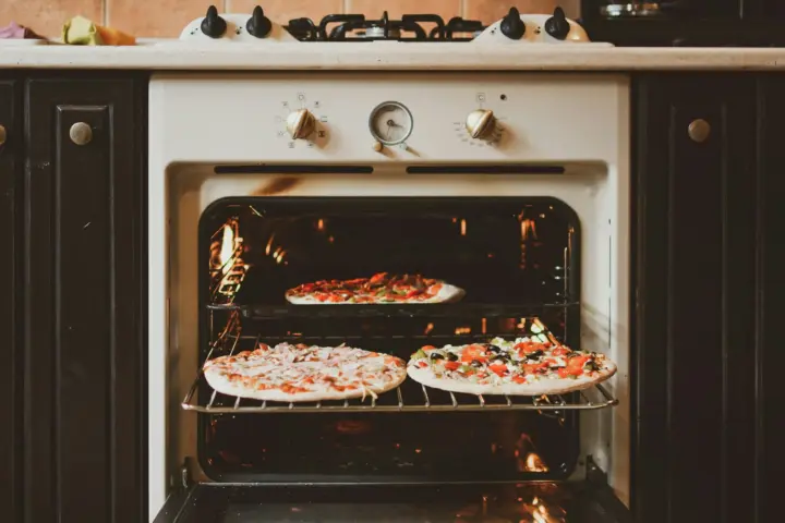 Three homemade pizzas baking on two racks of an open home oven, the heating element glowing at the top