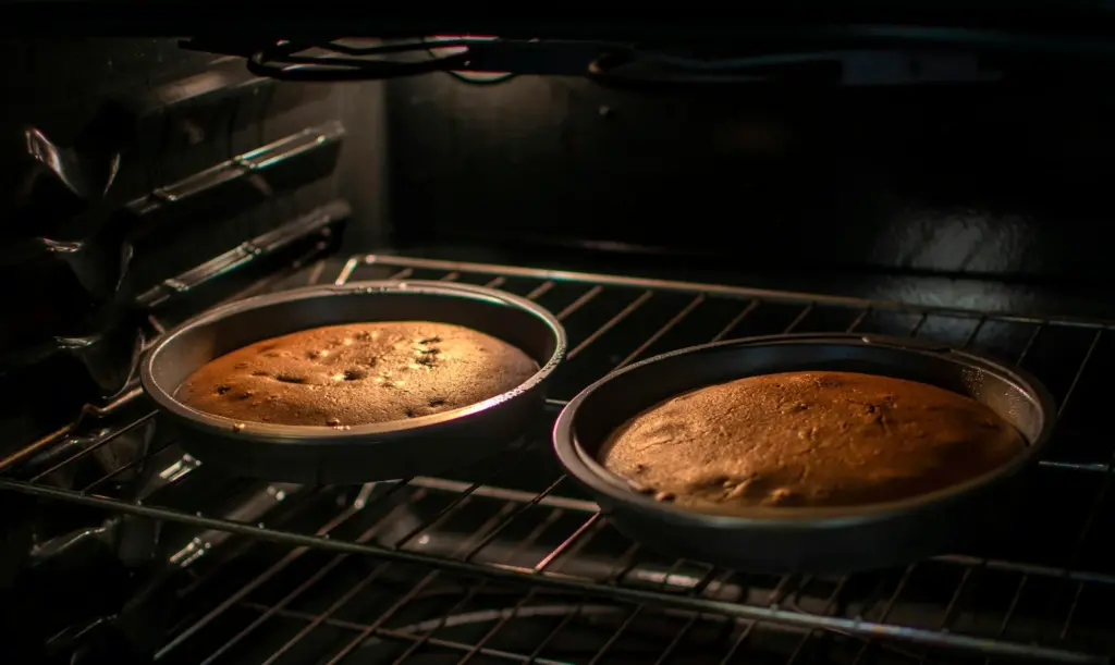 Two cake pans baking on the middle rack of a home oven, with an empty rack set higher above them