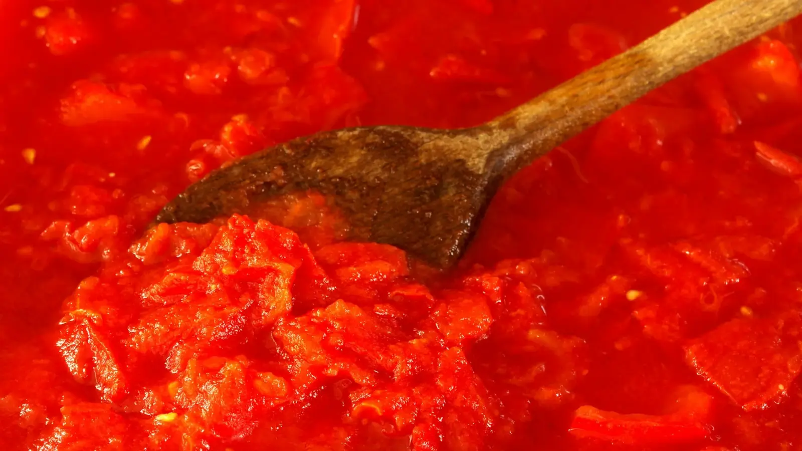 Chunky, bright red crushed tomato sauce with a wooden spoon resting in it