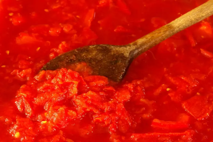 Chunky, bright red crushed tomato sauce with a wooden spoon resting in it
