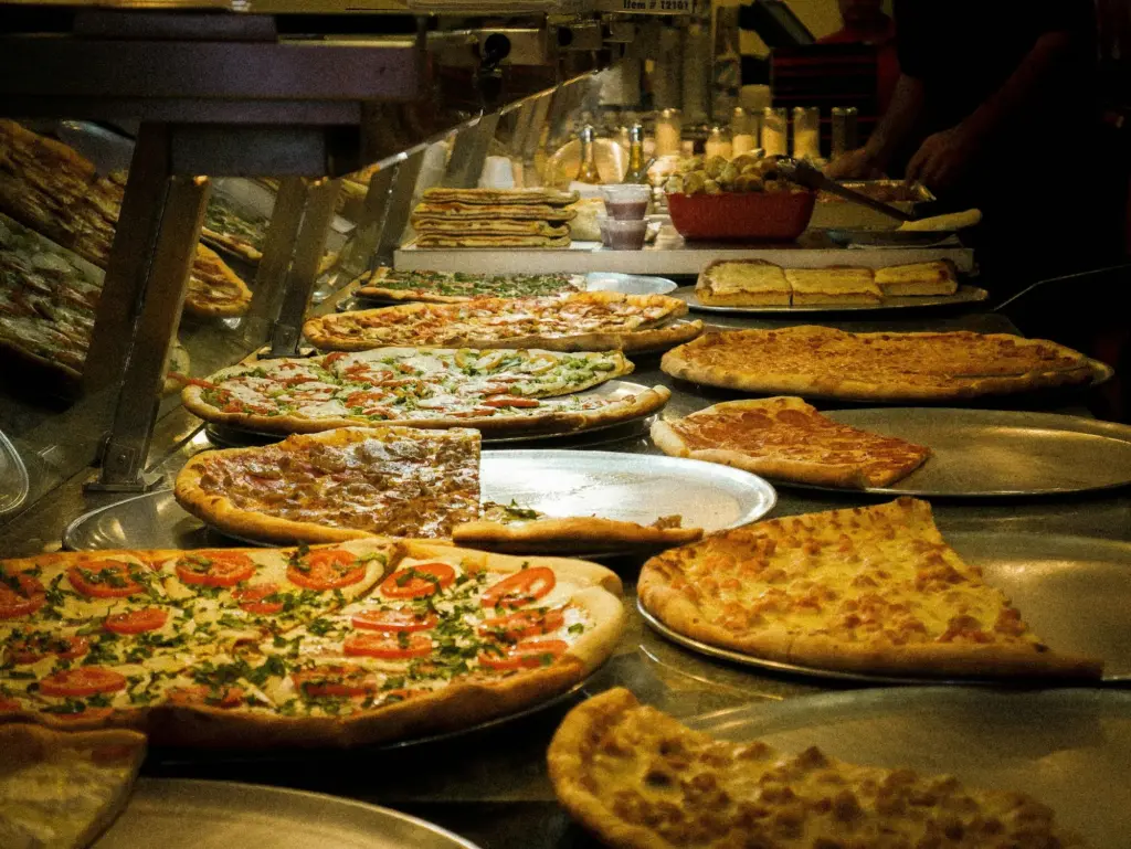 Whole thin-crust pies and partly sold pizzas on metal trays along a pizzeria counter